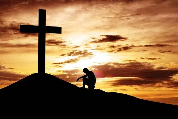 man kneeling at the cross at sundown