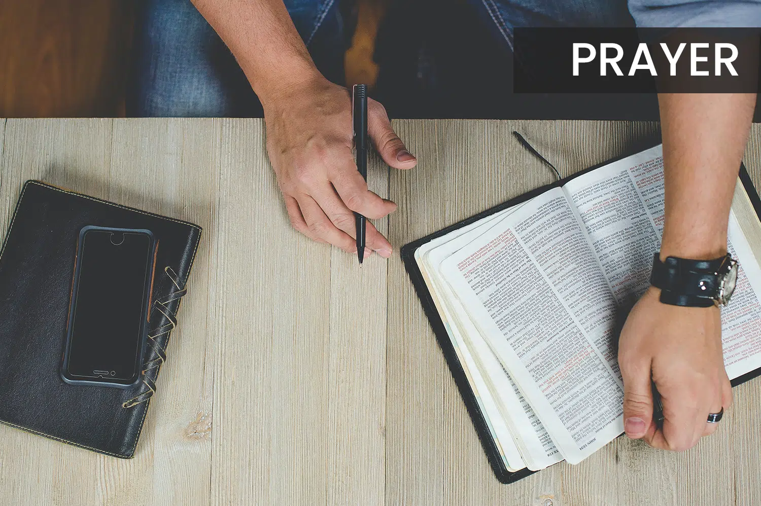 Anonymous man sitting at a table with an open Bible, getting ready to pray.